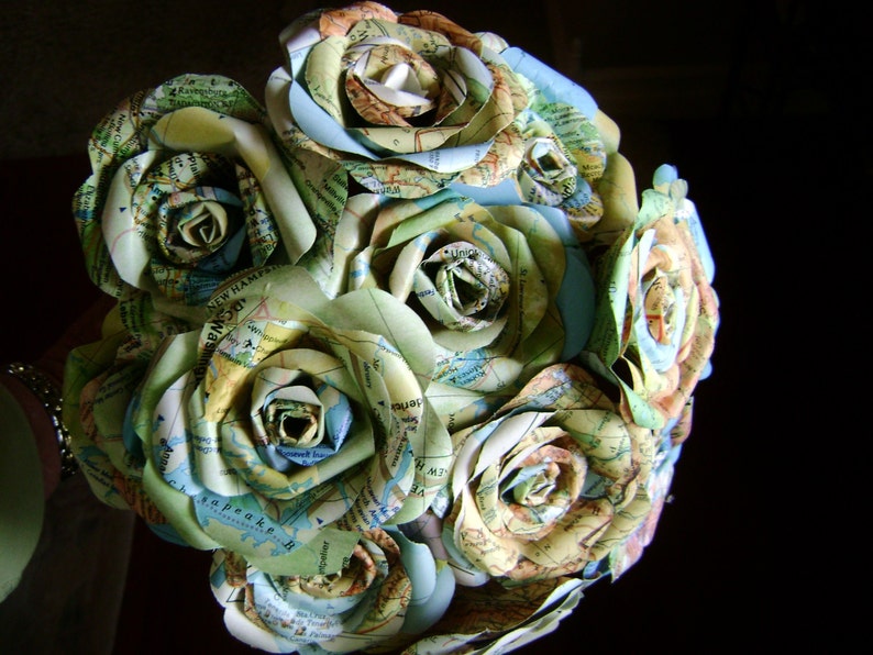 May include: A bouquet of paper roses made from maps, featuring shades of green, blue, and beige. The roses are arranged in a circular shape, creating a unique and artistic floral arrangement.