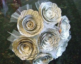 May include: A bouquet of paper flowers made from book pages. The flowers are white and have a delicate, vintage look. The bouquet is tied with a white ribbon and has a tulle overlay.