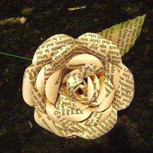 May include: A white paper rose made from pages of a book. The rose is made of several layers of paper, each with text printed on it. The rose is a delicate and intricate piece of art.