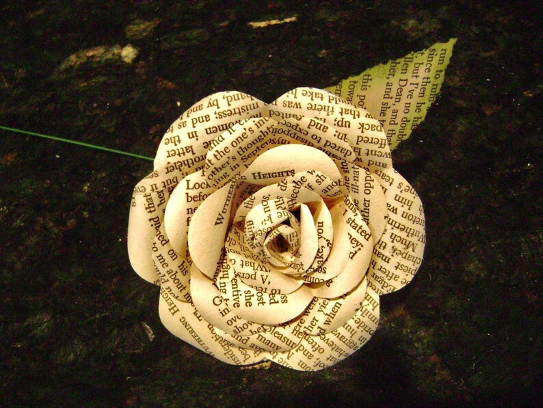May include: A white paper rose made from pages of a book. The rose is made of several layers of paper, each with text printed on it. The rose is a delicate and intricate piece of art.