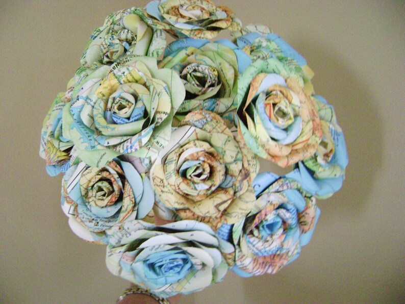 May include: A bouquet of paper roses made from maps in shades of blue, green, and brown. The roses are arranged in a circular shape and are tied together with a ribbon.