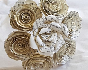 May include: A bouquet of seven paper roses made from recycled book pages. The roses are cream colored and have a vintage look.