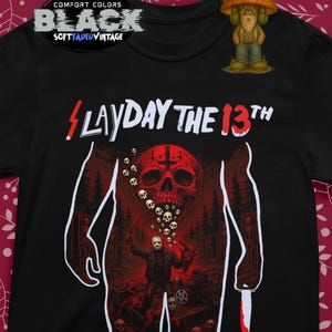 以下が含まれることがあります： 「SLAYDAY THE 13TH」の文字と、頭蓋骨、マスクをつけた人物、血まみれのナイフのグラフィックが描かれた黒いTシャツ。「COMFORT COLORS」と「BLACK SOFT FADED VINTAGE」の文字も含まれています。