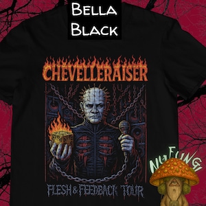 Puede incluir: Camiseta negra con un gráfico que presenta un personaje con alfileres en la cabeza, sosteniendo un cubo y un micrófono. El texto "CHEVELLERAISER" está encima del personaje, con "FLESH & FEEDBACK TOUR" debajo. Un gráfico de hongo está en la parte inferior derecha.
