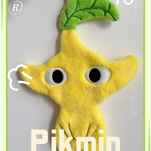Könnte beinhalten: Ein gelbes Pikmin-Plüschtier mit einem grünen Blatt, schwarzen Augen und dem Wort "Pikmin" in weißen Buchstaben. Das Spielzeug ist etwa 35 cm hoch und hat eine weiße Schnur zum Aufhängen.