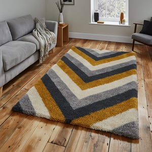 May include: A contemporary rug with a zig-zag design. The rug has bands of grey, cream, and ochre yellow. It is positioned on a wooden floor in a living room, complementing the neutral decor.