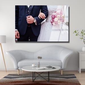 Peut inclure: Impression photo de mariage avec un couple. Le mari&eacute; porte un costume bleu marine et une montre-bracelet. La mari&eacute;e est v&ecirc;tue d'une robe de mari&eacute;e blanche et tient un bouquet de roses roses et blanches. L'image est affich&eacute;e sur un mur.