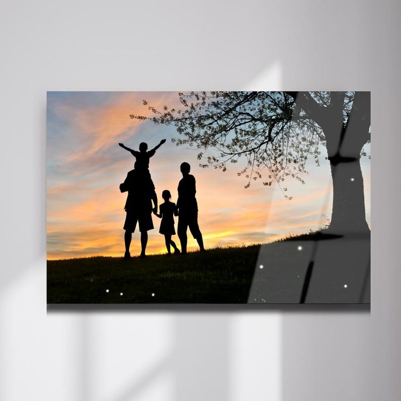 Peut inclure: Impression encadr&eacute;e d'une famille silhouett&eacute;e contre un coucher de soleil vibrant. Un enfant est assis sur les &eacute;paules d'un parent, les bras lev&eacute;s. Un autre enfant tient la main d'un adulte. Un arbre est en arri&egrave;re-plan.