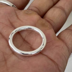 May include: A polished silver band ring with a smooth, rounded surface. The ring features a simple, circular design with a reflective metallic finish, showcasing a clean and uniform appearance throughout the entire circumference of the band.