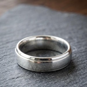 May include: A polished silver-toned band ring featuring a smooth, rounded surface with a subtle horizontal groove detail running along the center. The text SIMPLE SOUL MADE is displayed in a serif font above the ring.