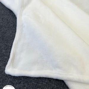 May include: A soft, white fleece blanket. The blanket is folded, showing a corner with a stitched edge. The fabric appears plush and cozy. The blanket is likely for home use, providing warmth and comfort. The logo "JeremyTans" is visible in the corner.