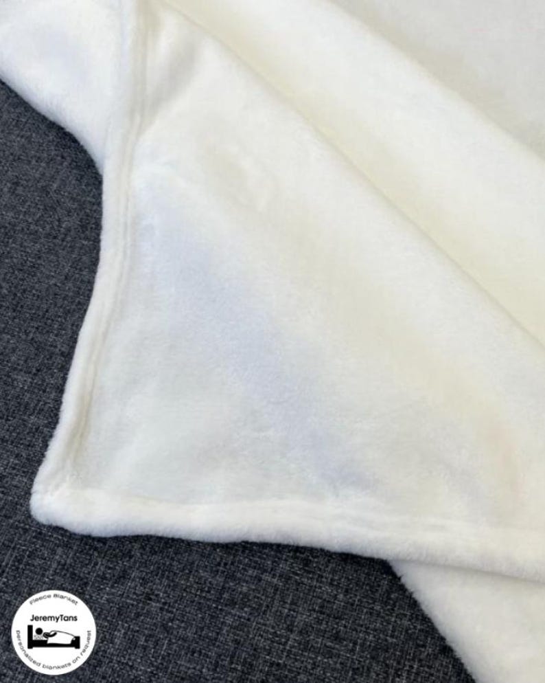 May include: A soft, white fleece blanket. The blanket is folded, showing a corner with a stitched edge. The fabric appears plush and cozy. The blanket is likely for home use, providing warmth and comfort. The logo "JeremyTans" is visible in the corner.
