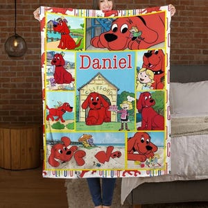 May include: A red and white fleece blanket featuring cartoon images of a large red dog. The blanket has a yellow border and the name "Daniel" in red letters. The blanket is held up by a person.