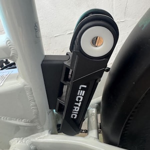 May include: A black "LECTRIC" brand bike lock mounted on a white bike frame. The lock is closed, with a white circular end and a keyhole. The bike has a black fender and a black tire.