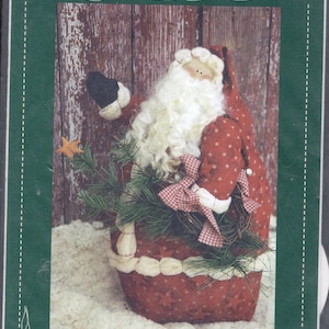 May include: A handmade Santa Claus doll, approximately 11 inches tall, with a red and white outfit. The doll has a white beard, a star-shaped ornament, and a green wreath. The image has the text "Threads That Bind" and "Jolly".