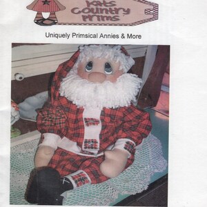 May include: A handmade Santa Claus doll with a red and black plaid outfit, white beard, and rosy cheeks. The doll is sitting on a white lace doily. The image includes the text "#121 Patches Santa."
