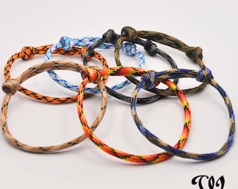 May include: A collection of six paracord bracelets in various colors, including orange, blue, brown, and camouflage patterns. Each bracelet features a knotted closure and a circular design, suitable for everyday wear.