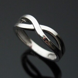 May include: A silver infinity ring with a smooth, polished finish. The ring is designed with two intertwined bands that create a continuous loop.