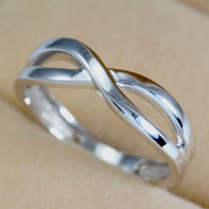 May include: A silver infinity ring with a polished finish. The ring is made of two intertwined bands that form a continuous loop.