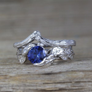 Puede incluir: Un anillo de plata con una piedra preciosa de zafiro azul, con un dise&ntilde;o de rama y hojas.