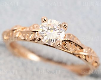 May include: A rose gold engagement ring with a round, clear center stone and a delicate, leaf-shaped band.