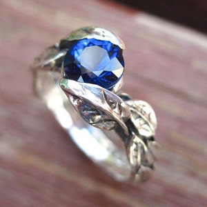 Puede incluir: Un anillo de plata con una piedra preciosa de zafiro azul engastada en un dise&ntilde;o de hojas.