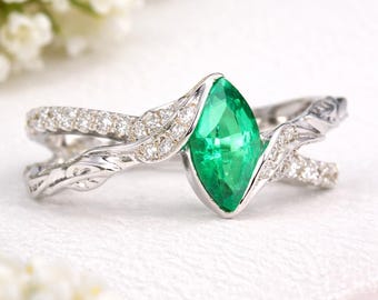 Könnte beinhalten: Ring mit einem Smaragd im Marquiseschliff und einem Weißgoldband. Der Smaragd ist ein leuchtendes Grün und in einer Krappenfassung gefasst. Das Band hat ein verdrehtes Design mit kleinen, funkelnden Diamanten. Feiner Schmuck.