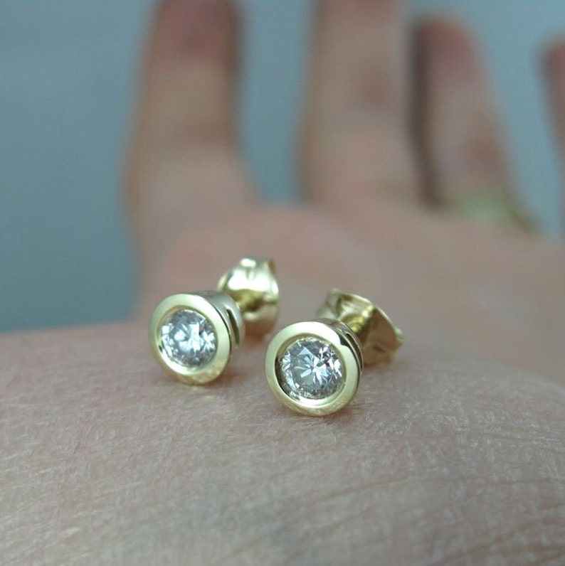 May include: A pair of gold stud earrings with round, clear gemstones.