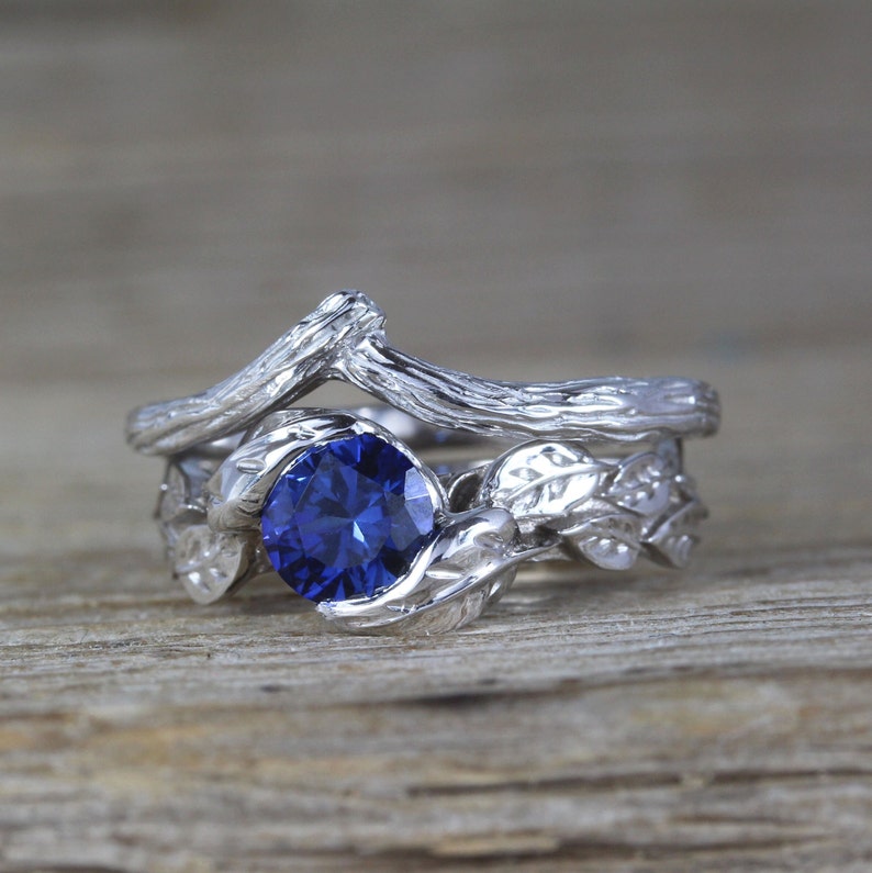 Puede incluir: Un anillo de plata con una piedra preciosa de zafiro azul, con un dise&ntilde;o de rama y hojas.