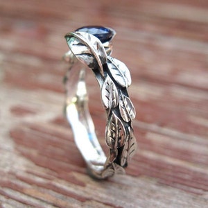 Puede incluir: Un anillo de plata con una piedra preciosa azul y un dise&ntilde;o de hojas alrededor de la banda.