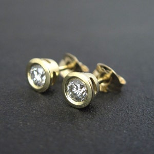 May include: A pair of gold stud earrings with round, clear gemstones.