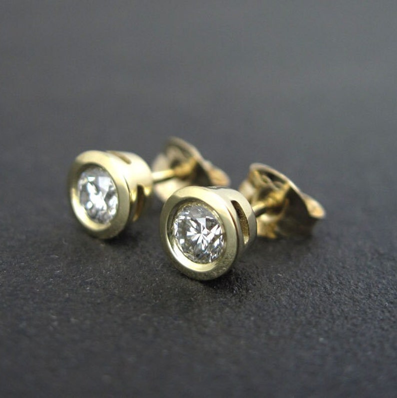 May include: A pair of gold stud earrings with round, clear gemstones.