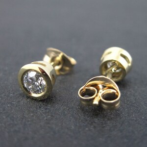 May include: A pair of gold stud earrings with a round, clear diamond in each earring.