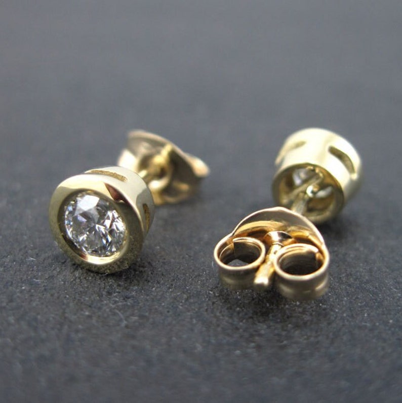 May include: A pair of gold stud earrings with a round, clear diamond in each earring.