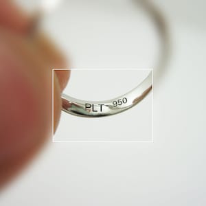 May include: Close-up of the inside of a silver ring with the inscription "PLT 950" engraved on the band.