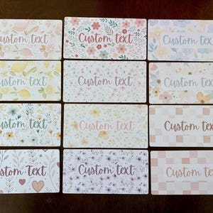 May include: A collection of rectangular cards with floral and fruit patterns, including lemons, flowers, and hearts. Each card features the text "Custom Text" in a script font, with a watercolor effect. The cards are arranged on a brown surface.