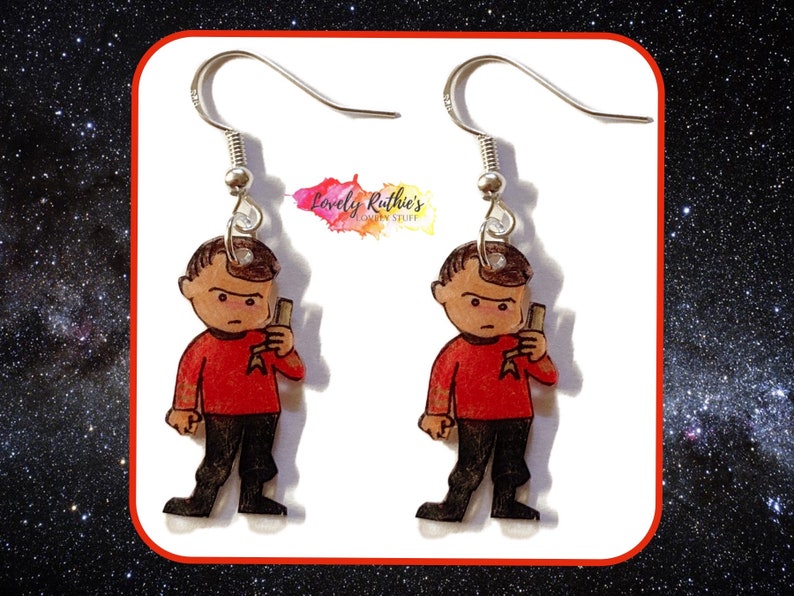 Puede incluir: Un par de pendientes con un personaje de dibujos animados con una camisa roja, pantalones negros y un phaser. El personaje es de la franquicia Star Trek.