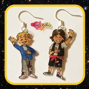 May include: A pair of earrings featuring cartoon characters. The character on the left is wearing a blue jacket, grey trousers, and a red and white shirt. The character on the right is wearing a black waistcoat, black shorts, a red belt, and a white shirt. Both characters are smiling.