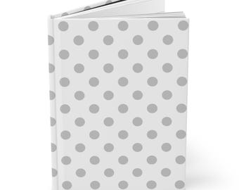 May include: A hardcover journal with a white cover featuring a pattern of evenly spaced gray polka dots. The journal is open, revealing the blank pages inside. The spine is white.