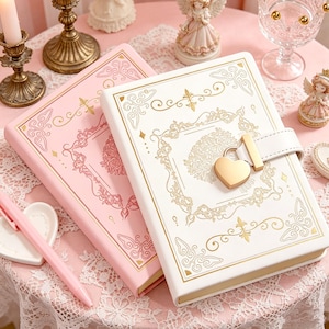 May include: Two decorative journals with gold detailing. One is white with a heart-shaped lock, the other is pink. Both have gold floral patterns and are closed with a strap.
