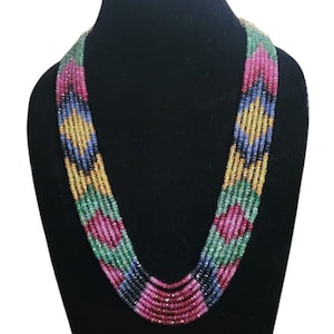 Op de afbeelding: Een ketting met meerdere strengen met een levendige reeks kleuren, waaronder rode, roze, groene, gele, blauwe en zwarte kralen. De ketting wordt getoond op een zwarte mannequin, die het ingewikkelde ontwerp en het kleurenpatroon benadrukt.