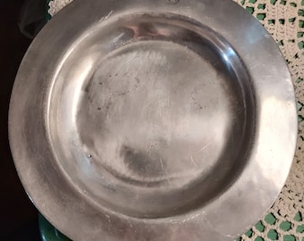 May include: A silver metal plate with a raised rim and a small, circular mark in the centre.
