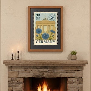 May include: Framed print featuring a vintage German postage stamp design. The stamp depicts the Brandenburg Gate, blue flowers, and the word "GERMANY". The print is displayed above a stone fireplace with lit candles and a small plant.
