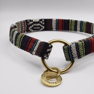 May include: A black and white striped fabric dog collar with a gold metal ring and a gold metal tag that says "SINCLAIR" on it.