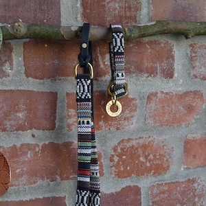 May include: Two dog collars with a black and white geometric pattern. One collar is a leash with a black leather strap and a brass ring. The other collar is a shorter collar with a brass tag that reads "REILLY".