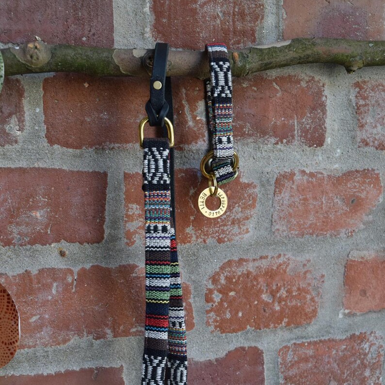 May include: Two dog collars with a black and white geometric pattern. One collar is a leash with a black leather strap and a brass ring. The other collar is a shorter collar with a brass tag that reads "REILLY".