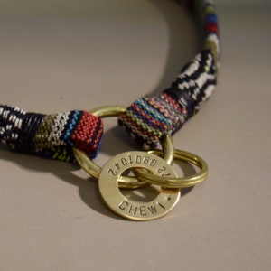 May include: A colorful woven dog collar with a brass tag engraved with the text "CHEWI" and the numbers "22 660 1042".