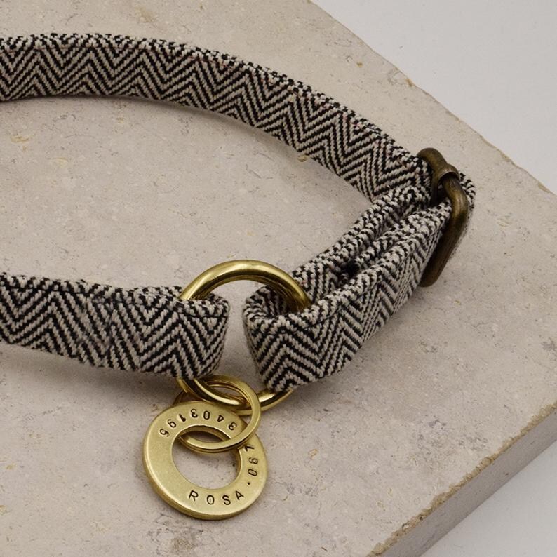 May include: A pet collar featuring a black and white chevron pattern fabric strap with an antique brass metal buckle and a circular brass tag engraved with the name ROSA and the numbers 3403195, attached to a brass ring on the collar strap.