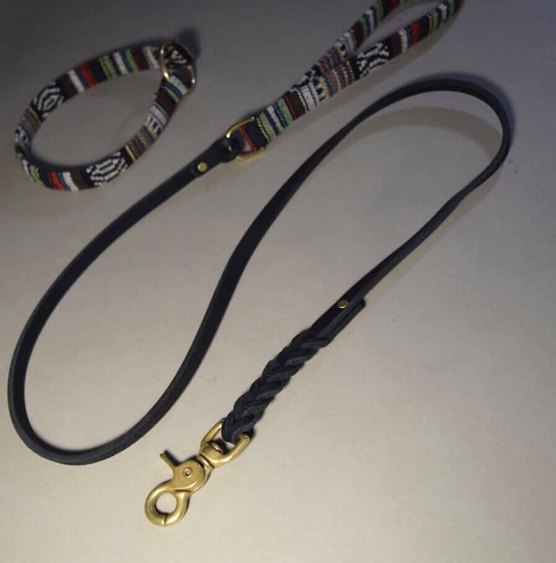 May include: A black leather dog leash with a braided section and a brass clasp. A matching black and white patterned collar is also visible.