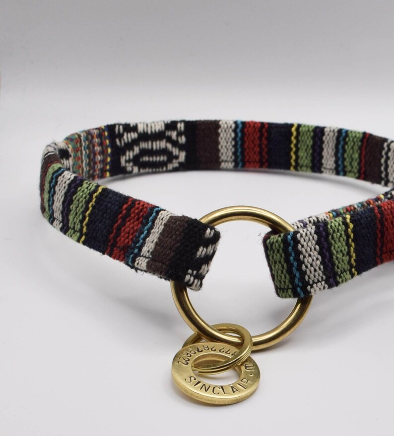 May include: A black and white striped fabric dog collar with a gold metal ring and a gold metal tag that says "SINCLAIR" on it.